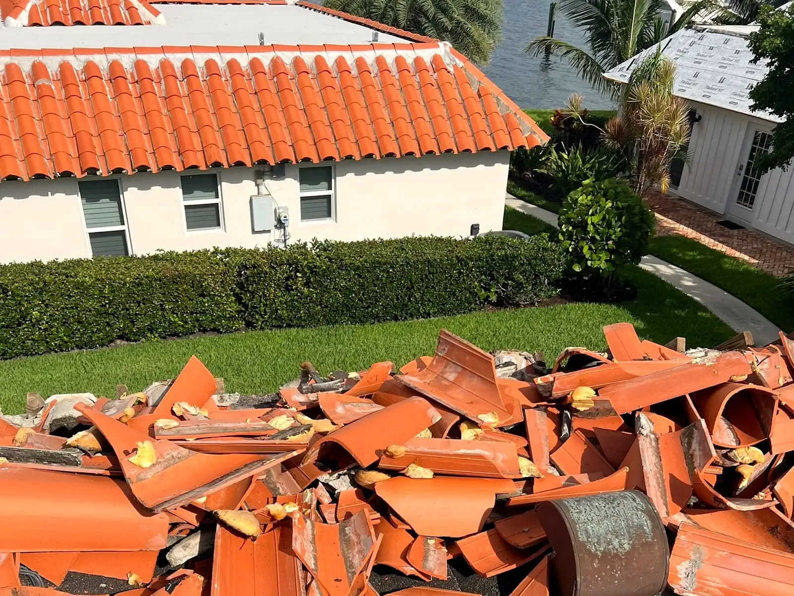 Old clay tile torn off a roof and piled for removal, with a tile-roofed house and the water beyond